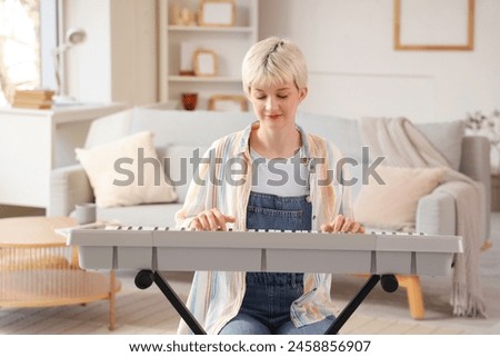 Young woman with short hair playing synthesizer at home Royalty-Free Stock Photo #2458856907