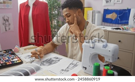 An african american man sketches fashion designs in a colorful tailor shop, surrounded by sewing equipment and fabric samples.