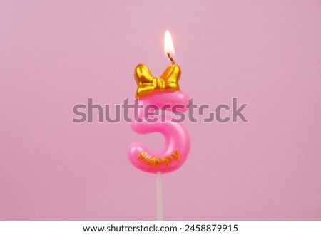 Burning pink birthday candle with golden bow and word happy on pink background, number 5.
