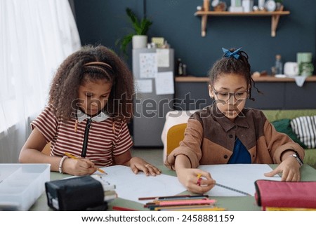 Portrait of two Black girls drawing pictures together sitting at table at home