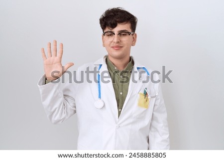 Young non binary man wearing doctor uniform and stethoscope showing and pointing up with fingers number five while smiling confident and happy. 