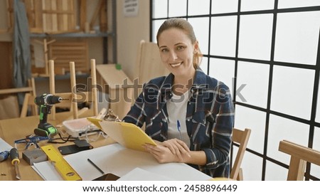 Smiling woman in a woodworking studio surrounded by carpentry tools posing confidently for a stock photo.
