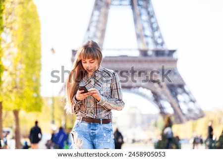 Happy girl using phone in Paris with Eiffel Tower on background - Blonde young woman walking and looking at her smartphone - Travel and lifestyle concepts