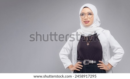 Portrait of Muslim woman in office attire and wearing a hijab. Corporate  or business people concept. Isolated on grey background. 16:9 ratio with copyspace on one side of the banner Royalty-Free Stock Photo #2458917295