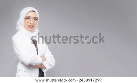 Portrait of Muslim woman in office attire and wearing a hijab. Corporate  or business people concept. Isolated on grey background. 16:9 ratio with copyspace on one side of the banner Royalty-Free Stock Photo #2458917299