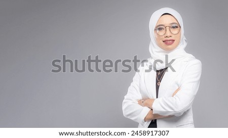 Portrait of Muslim woman in office attire and wearing a hijab. Corporate  or business people concept. Isolated on grey background. 16:9 ratio with copyspace on one side of the banner Royalty-Free Stock Photo #2458917307