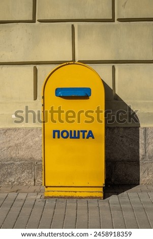 A yellow post box on a street in Ukraine with a Ukrainian inscription