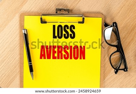 LOSS AVERSION text on a yellow paper on clipboard with pen and glasses.  Royalty-Free Stock Photo #2458924659