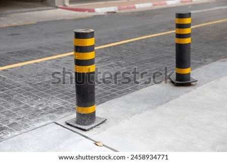Two yellow and black steel bollards are on the sidewalk