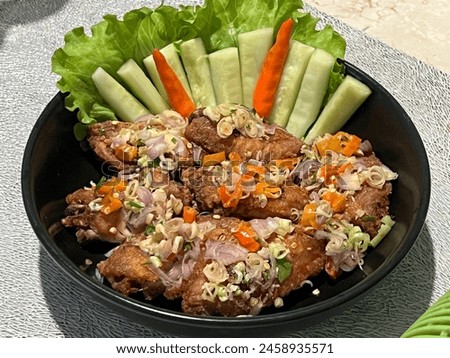 A picture of Indonesian food called “Ayam Geprek” which is a crispy battered fried chicken crushed and mixed with hot and spicy sambal in a black bowl garnished with vegetable and chili