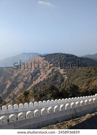 The picture shows a peaceful scene of a mountain range with a stone wall and a winding pathway.