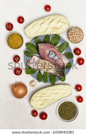 Pieces of river carp fish in plate. Eggplant, tomatoes and  groats on table. White background. Flat lay.
