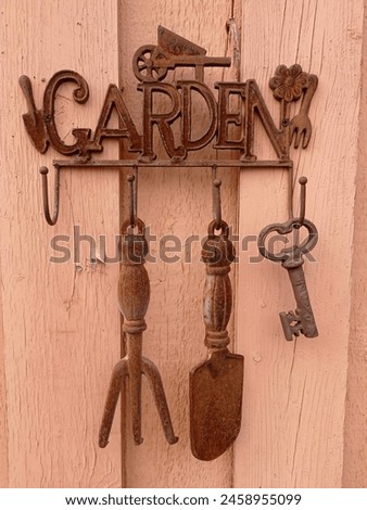 Garden decoration. A rusty sign that says garden and some decorative gardening tools hanging on the old, painted wall.