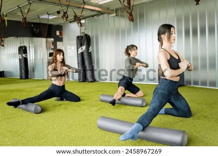 A group of 3 adult women are doing a Pilates class in a gym room.The three girls are doing a balance exercise with a foam roller.Concept of women performing pilates with accessories.
