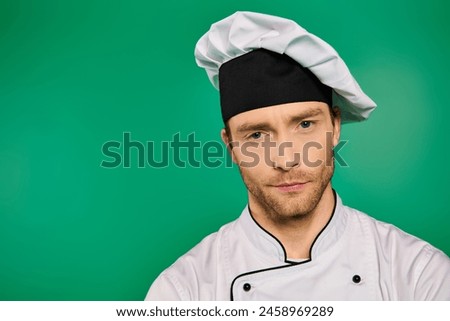 A handsome male chef in a white uniform posing for a picture on a green backdrop.