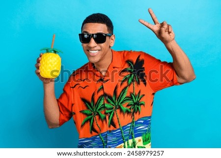Photo of cool funky guy dressed print shirt enjoying pineapple juice showing v-sign isolated blue color background