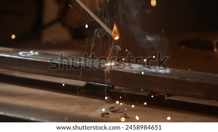 Metalworker using welding machine on iron surface, smoke, sparks and flashing lights around, man worker welding steel material. Close up shot.