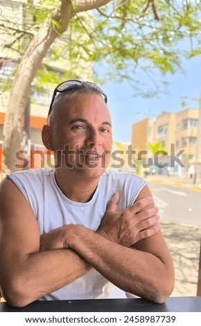 Portrait of handsome young adult man, with arms folded, sitting at the bar looking ahead smiling, taking a selfie. Being in good company. Chatting with friends