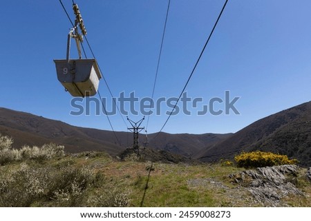 Abandoned industrial coal mining cart on cableway with rusty metal tower with cable on a bright sunny spring day with flower meadow and blue sky Royalty-Free Stock Photo #2459008273