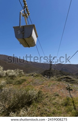 Abandoned industrial coal mining cart on cableway with rusty metal tower with cable on a bright sunny spring day with flower meadow and blue sky Royalty-Free Stock Photo #2459008275
