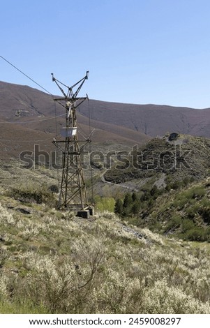Abandoned industrial coal mining cart on cableway with rusty metal tower with cable on a bright sunny spring day with flower meadow and blue sky Royalty-Free Stock Photo #2459008297