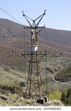 Abandoned industrial coal mining cart on cableway with rusty metal tower with cable on a bright sunny spring day with flower meadow and blue sky Royalty-Free Stock Photo #2459008303