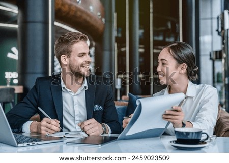 Two business colleagues discussing over a report document at work. Business man and woman having a meeting in office lobby. Happy young female employee showing project to skilled team leader
