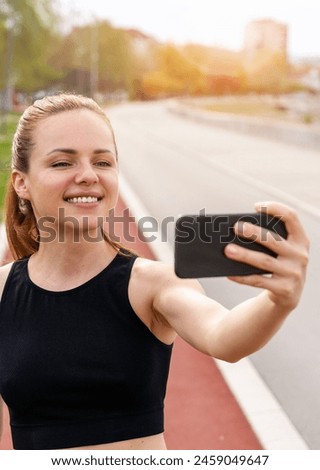Brunette woman wearing sportswear takes a selfie while running on running track in city.