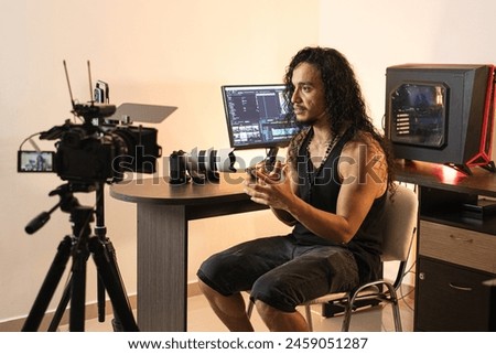 Online Content Creator Studio. A long-haired content creator immersed in his studio, recording videos with his phone mounted on a tripod. Cameras, lights, and a computer are part of his setup