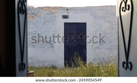 Inside a gateway, a view unveils an old house's heart, lush with grass. Time-worn walls echo tales, while nature's embrace whispers serenity. Royalty-Free Stock Photo #2459054549