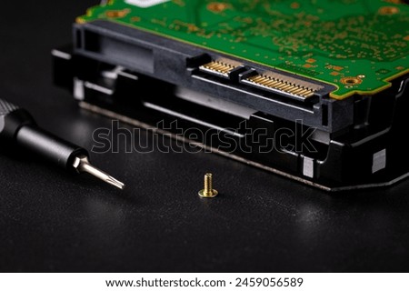 Hard disk drive and printed circuit board with SATA power connector. Magnetic driver torx bit and small machine screw on dark background.