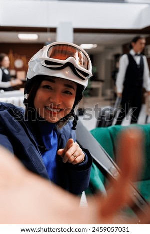 Youthful asian woman at exclusive ski resort holding cellphone for selfie picture. Enthuisiastic female traveler wearing winter jacket ski goggles and helmet ready for wintersport activities.