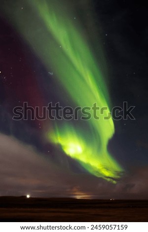 Aurora borealis over icelandic scenery, snowy mountains and glowing night sky filled with stars. Northern lights in Iceland forming magical winter landscape, green and yellow colors.