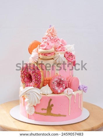 Pink layered tall cake with pink frosting, cake pops, macaroons, meringues, donuts and golden figure of gymnast girl