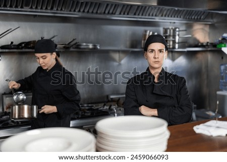 Confident woman executive chef standing in restaurant kitchen, posing on camera, while his team working Royalty-Free Stock Photo #2459066093