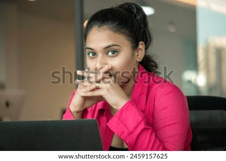 Image of young beautiful joyful Indian woman smiling while working with laptop in office.