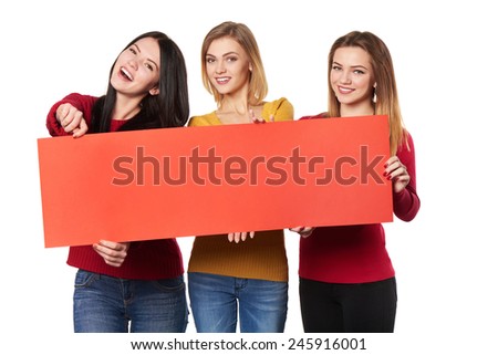 Three excited surprised girls friends showing red blank cardboard over white background