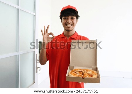 Smiling pizza deliveryman in red t-shirt holding an open pizza box and showing okay hand sign