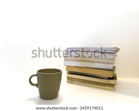 Coffee cup next to pile of books on white background. Creative photo.