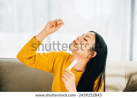 Highlighting COVID-19 self-test, Asian woman uses a rapid antigen test kit at home inserting a swab into her nose. Depicting virus prevention and pandemic protection measures. Royalty-Free Stock Photo #2459252843
