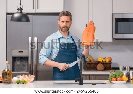 Hispanic man in cook apron hold salmon fillet at kitchen. Cooking salmon fillet. Restaurant menu with salmon fillet. Cooking, advertising salmon fillet concept. Cook in chef apron.