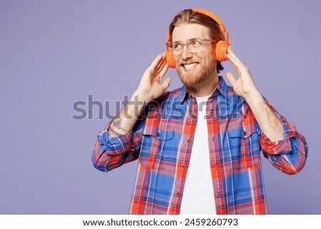 Young smiling cheerful happy man he wear blue shirt casual clothes listen to music in headphones look aside on area isolated on plain pastel light purple background studio portrait. Lifestyle concept
