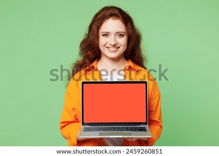 Young smiling happy ginger IT woman wear orange shirt white t-shirt casual clothes hold use work on blank screen laptop pc computer isolated on plain pastel light green background. Lifestyle concept
