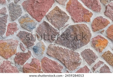 It's close up view of colorful wall. Its photo of multicolor stonewall. It is photo of multicolored srone wall. its view of red sidewalk. It's view of mosaic stonewall