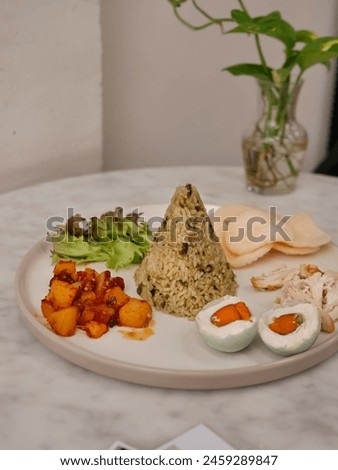 delicious and tasty nasi tumpeng hijau or green cone-shaped rice with sambal goreng kentang or potato fried chili, shredded chicken and salted egg on a plate. Indonesian traditional cuisines Royalty-Free Stock Photo #2459289847