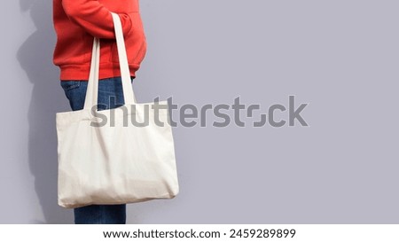 Woman in red hoodie holding tote canvas blank eco bag on street grey minimal wall background. Female consumer hold white textile shopper. template or place for your design, logo, text