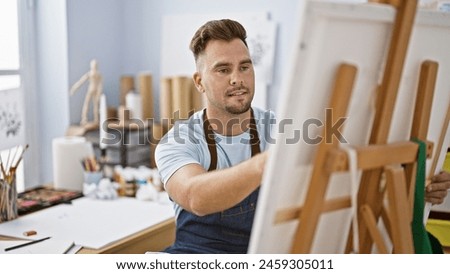 Handsome young man painting on a canvas in a well-lit art studio, portraying creativity and concentration.