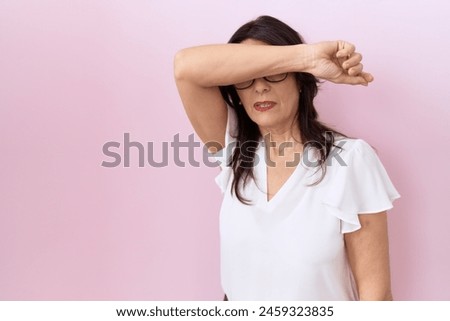 Middle age hispanic woman wearing casual white t shirt and glasses covering eyes with arm, looking serious and sad. sightless, hiding and rejection concept  Royalty-Free Stock Photo #2459323835