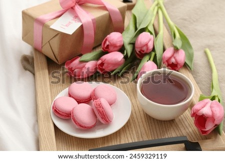 Tasty breakfast served in bed. Delicious macarons, tea, flowers, gift box and card with phrase I Love You on tray