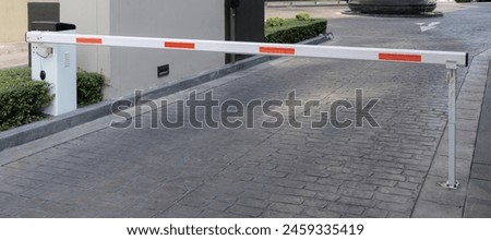 A white and orange traffic barrier is on a brick road. The barrier is in front of a building. automatic barrier bar.